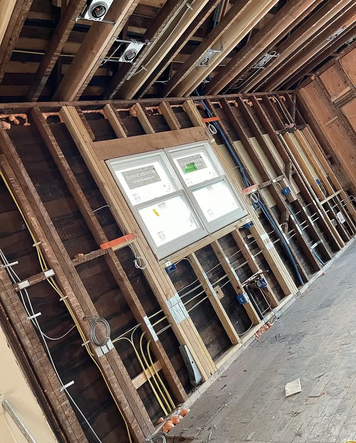 Open stud wall with blue device boxes at outlet height, yellow cables stapled down the studs and pot light housings in the ceiling joists