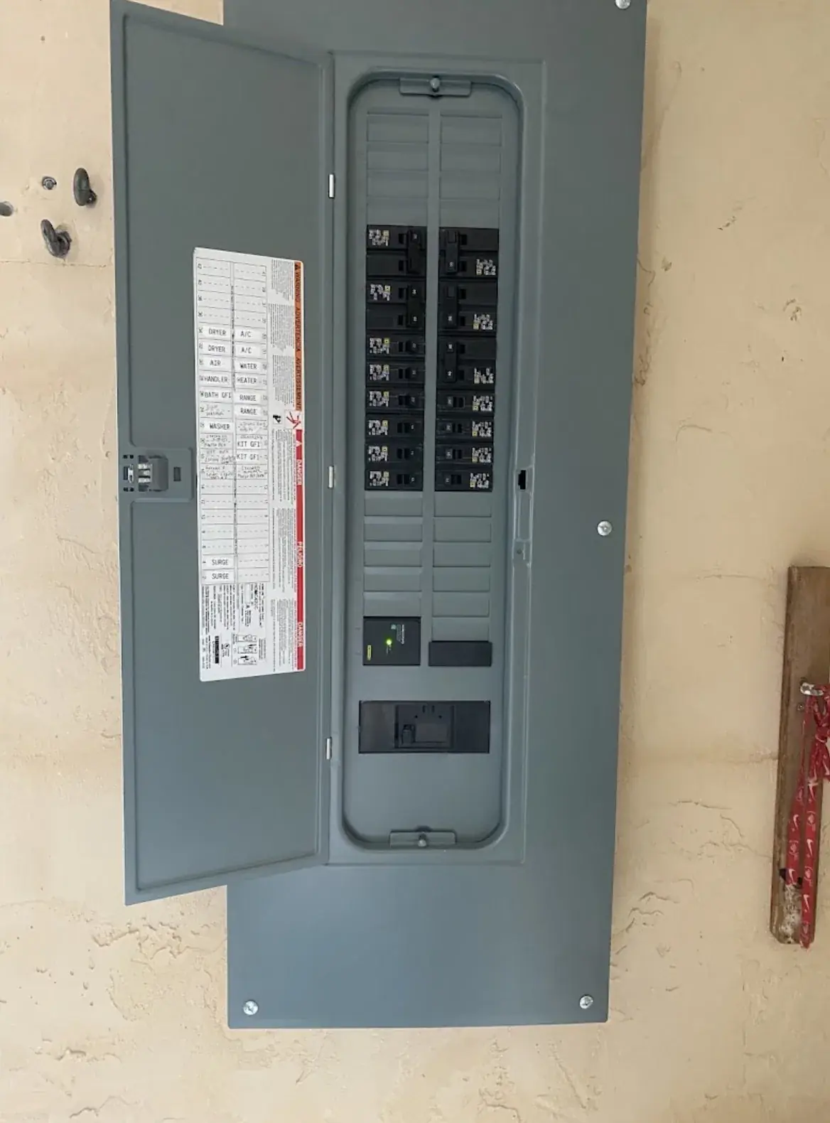 Grey breaker panel with the door open showing the circuit directory on the inside of the door and two columns of breakers